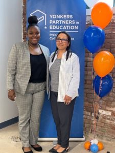 Nay Wasicsko and Mia Williams stand in front of a Yonkers Partners in Education sign.